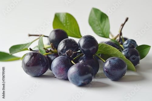 A bunch of plums with leaves, alongside blueberries, is displayed on a white surface.