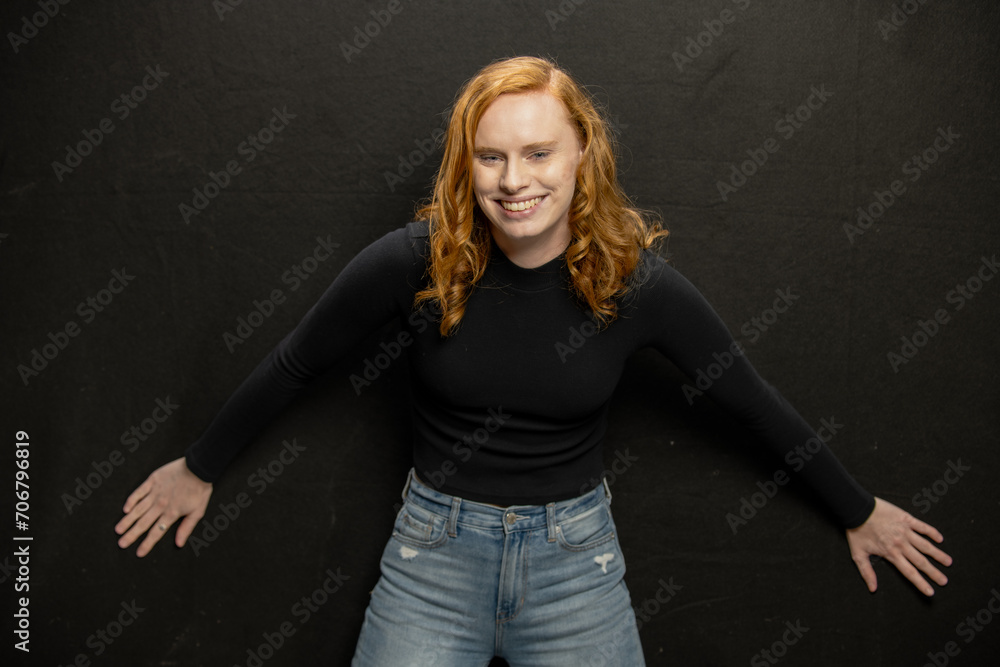 Young woman with red hair in black sweater and jeans poses in studio before a black background Young woman with red hair in black sweater and jeans poses in studio before a black background