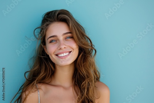 Portrait of a smiling young woman with flowing hair, against a soft blue background. photo
