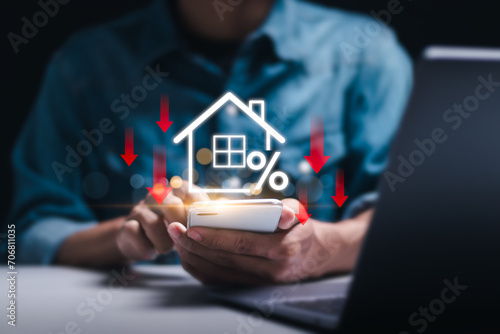 Businessman use smartphone with virtual home icon and down arrow for economical real estate and lower mortgage interest rates. Reduced prices for rental housing, Demand for home purchases decreases. photo