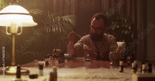 Male chemist mixing oils while creating perfume at table photo