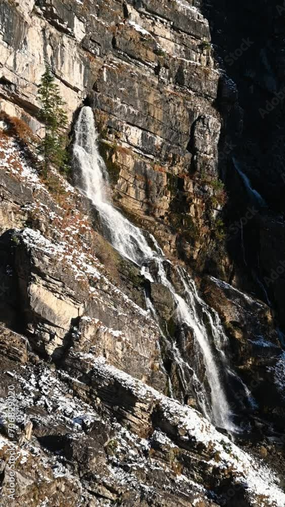 A karst spring in the middle of a wall in the mountains, evening sun in autumn, first snow, vertical shot, slow motion A karst spring in the middle of a wall in the mountains, evening sun in autumn, first snow, vertical shot, slow motion