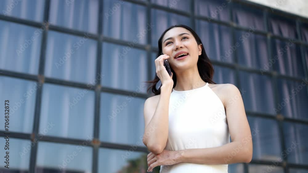 A confident Asian businesswoman stands talking on the phone with her business partner in the office outside outdoors using an application on a mobile phone fast connection online communication concept A confident Asian businesswoman stands talking on the phone with her business partner in the office outside outdoors using an application on a mobile phone fast connection online communication concept