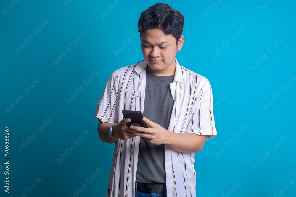 Smiling Asian man using smartphone over blue background Smiling Asian man using smartphone over blue background