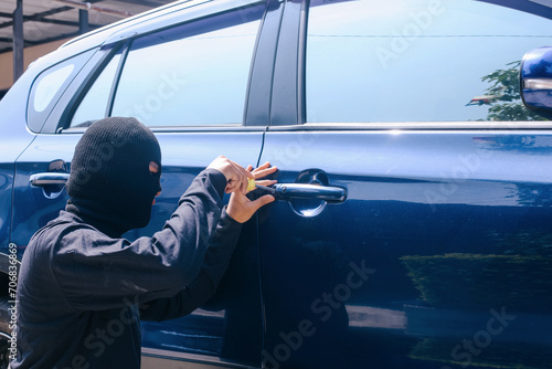 Theft with mask trying to break into the car using screwdriver. Street criminal and car theft concept. photo