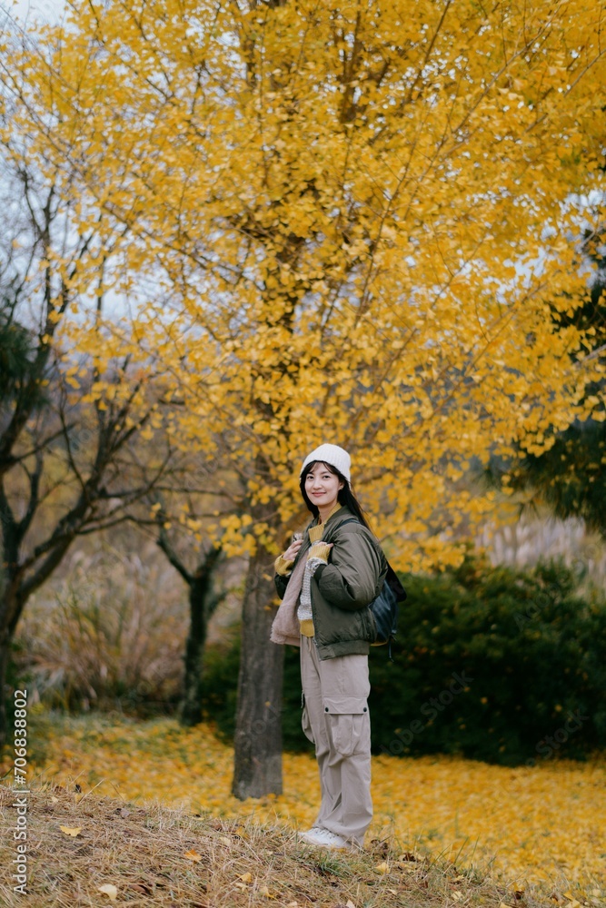 Asian woman in casual dress smiles amid colorful ginkgo leaves, embracing the beauty of the season. A joyful and relaxed portrait.