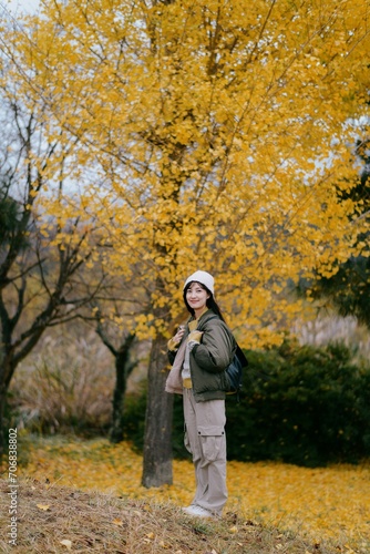 Asian woman in casual dress smiles amid colorful ginkgo leaves, embracing the beauty of the season. A joyful and relaxed portrait. © Jirawatfoto
