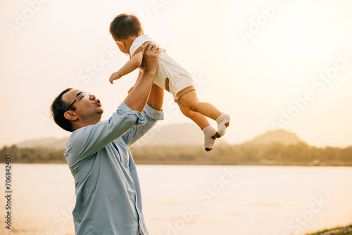 A happy dad and his toddler son share a playful moment of freedom and joy in the park, throwing him up in the air on a sunny summer day. Family love and happiness captured in a photograph photo