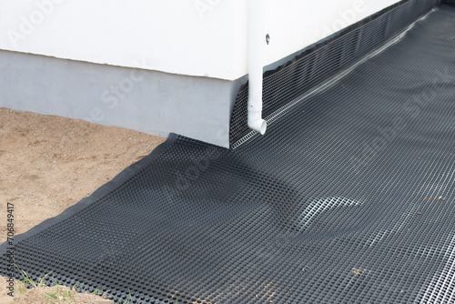 Laying a black waterproofing membrane around the foundation of a house. Construction of the blind area of the house. Reliable protection of the foundation from moisture. 