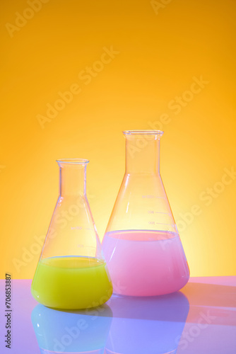 Color background with laboratory equipments decorated for advertising product. Erlenmeyer flasks containing color liquid on orange background. Front view