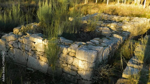 Golden hour light glistens on rock walls of old square fortified structure as wind blows grass photo
