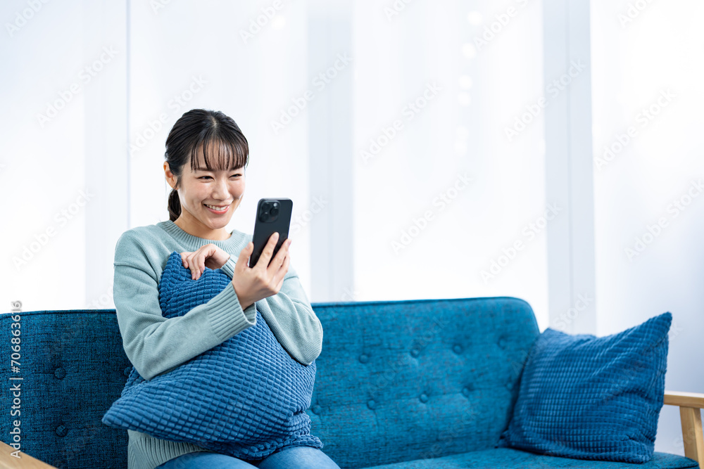 部屋のソファで携帯を持つ私服の若い女性