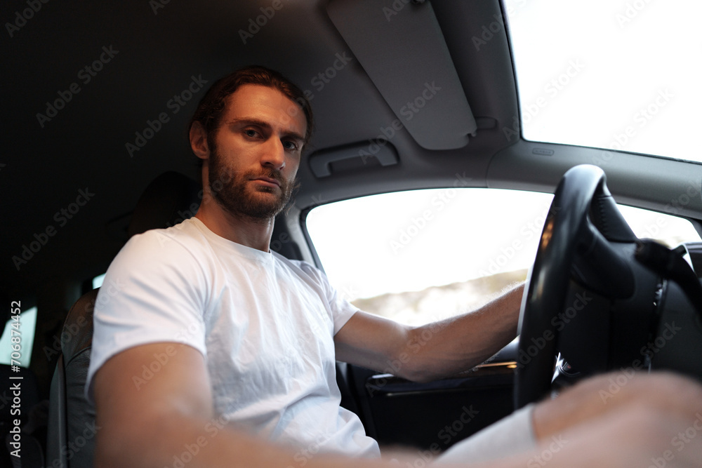 Bearded young man in casual t-shirt drives a car