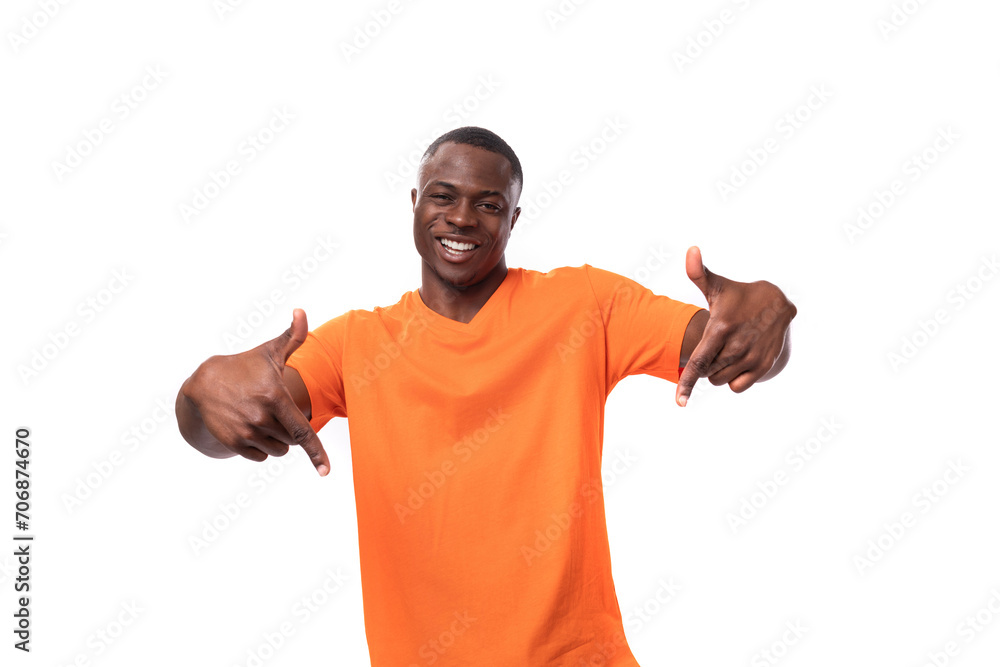 a young handsome american man dressed in an orange t-shirt points his finger in surprise at the empty space. corporate clothing concept a young handsome american man dressed in an orange t-shirt points his finger in surprise at the empty space. corporate clothing concept