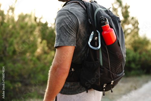 Obraz na plátně A male traveler backpack with mountaineering carabiner and thermos close up