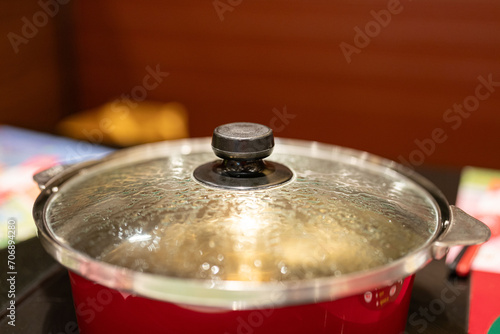 A hotpot kettle with boiling water is placed on the electric stove on the dining table. Close-up at the glass lid. Food utensil object photo. close-up and selective focus.