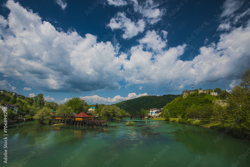 Fototapeta premium Bridge over Una river in Bosanska Krupa, looking towards some piers and fortress in the background. Beautiful scenery in bosnia, blue skies.