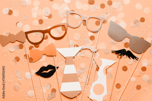 Photo booth props glasses, mustache, lips on a pink background flat lay. New trending PANTONE Peach Fuzz colour of 2024 year (ID: 706902443)