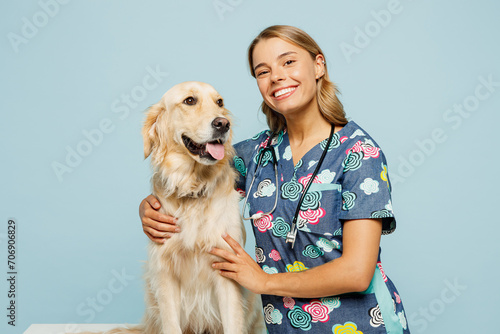 Young happy veterinarian woman wear uniform stethoscope heal exam hug cuddle embrace retriever dog look camera isolated on plain pastel light blue background studio portrait. Pet health care concept.