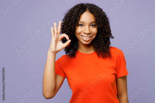 Little smiling happy cheerful kid teen girl of African American ethnicity wear orange t-shirt show okay ok gesture isolated on plain pastel light purple background studio. Childhood lifestyle concept. photo