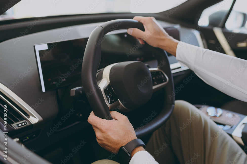 Cropped close up adult man customer buyer client wear shirt sit drive electric car hold steering wheel choose auto want to buy new automobile in showroom vehicle salon store motor show. Sales concept.