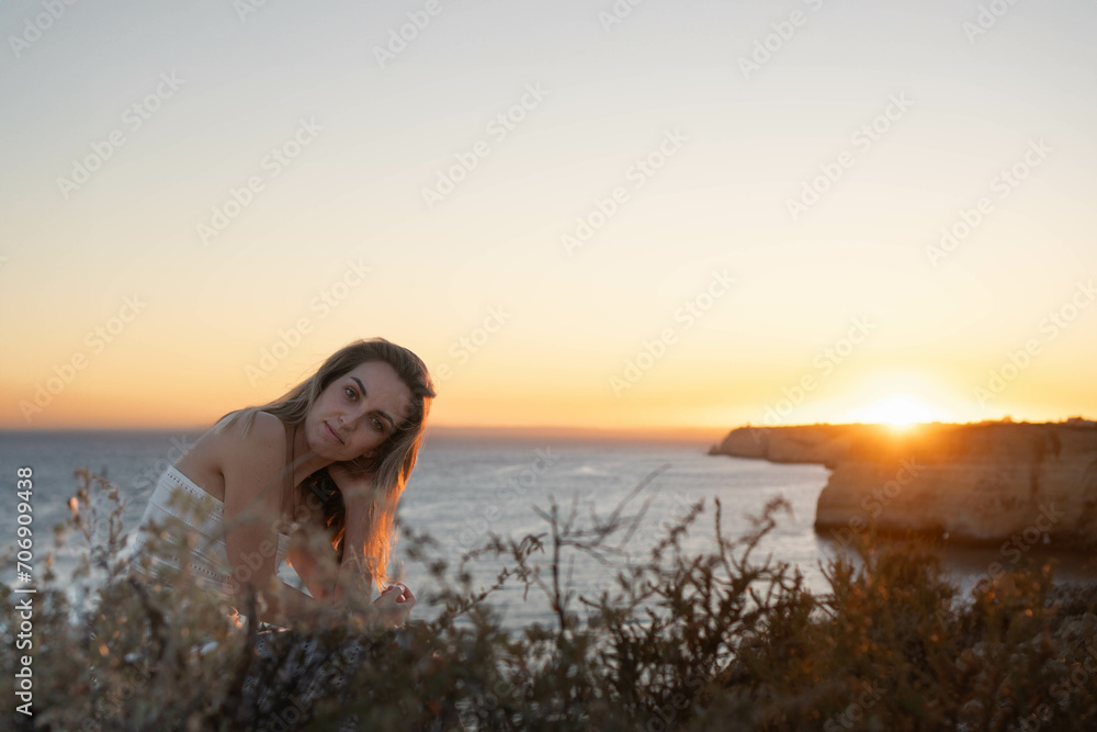 Woman sitting on slope against sunset and sea
