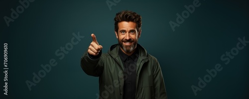 A bearded man, handsomely smiling, directs attention by pointing his finger towards something in front of him photo