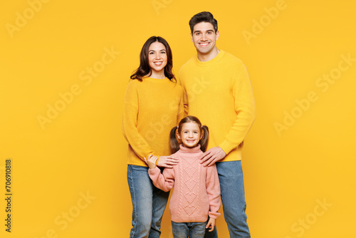 Full body young smiling cheerful happy parents mom dad with child kid girl 7-8 years old wear pink sweater casual clothes hug cuddle look camera isolated on plain yellow background Family day concept © ViDi Studio