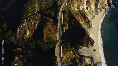 4k aerial footage of Bixby Creek Bridge on the Big Sur coast of California. Ocean waves at sunset by a rocky coast. A white car drives on a bridge along the coast. Road to the San Francisco 
