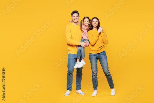 Full body young fun happy parents mom dad with child kid girl 7-8 years old wear pink sweater casual clothes hold little daughter look camera isolated on plain yellow background. Family day concept. © ViDi Studio