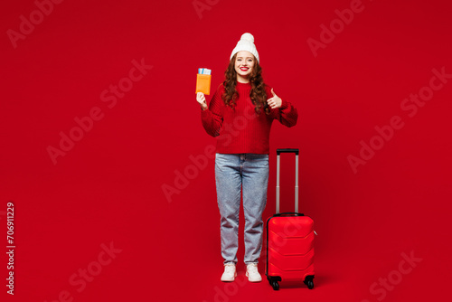 Traveler woman wear sweater hat casual clothes hold bag passport ticket show thumb up isolated on plain red background. Tourist travel abroad in free spare time rest getaway. Air flight trip concept. #706911229