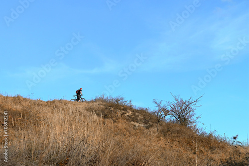 Cyclist riding a bike along sloping hill on a sunny day against a blue sky