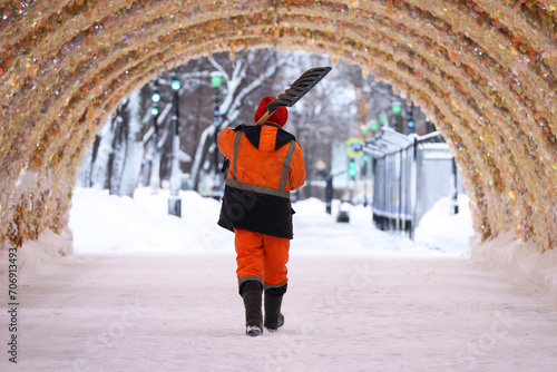 Canvas Print Worker with shovel walking on festive decorations, snow removal in winter city