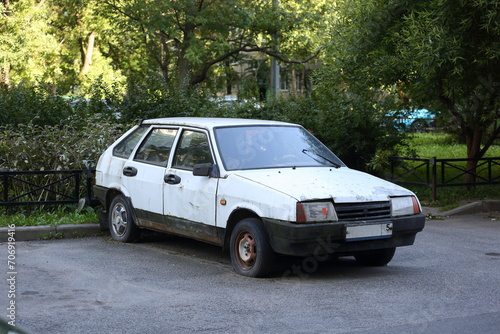 Old rusty white Russian car stands near the lawn, Ulitsa Antonova-Ovseenko, St. Petersburg, Russia, August 10, 2023