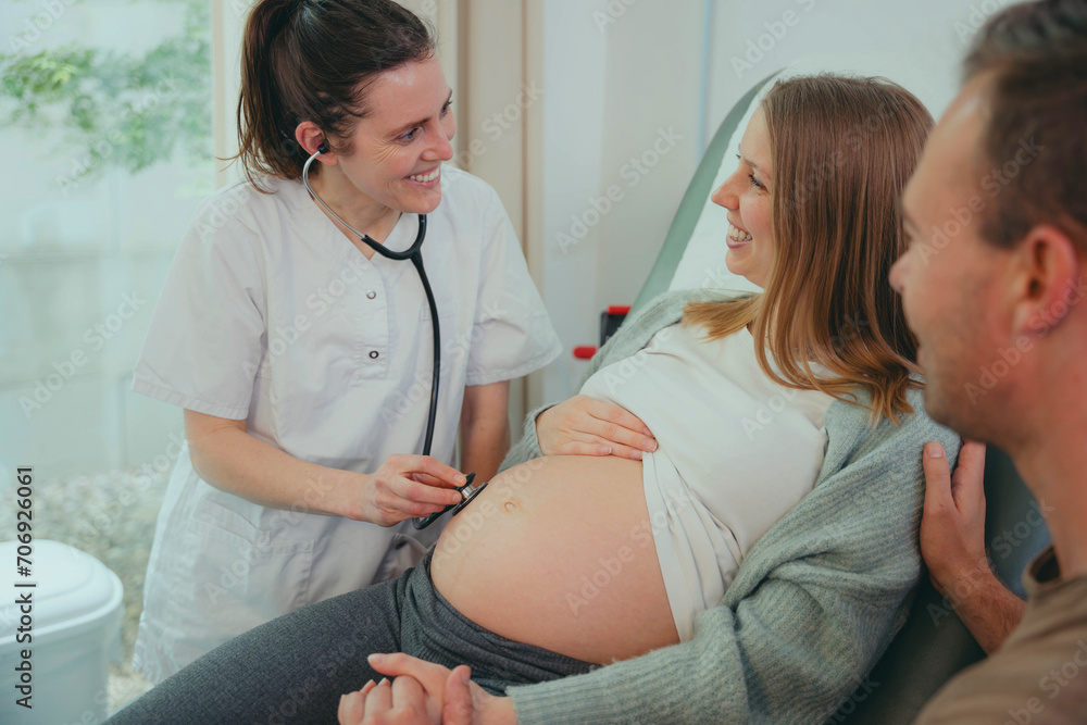 Obraz premium Happy pregnant woman visiting obstetrician doctor in maternity clinic - Female gynaecologist examining belly with stethoscope - Health care and medical concept