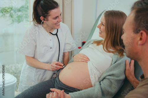 Happy pregnant woman visiting obstetrician doctor in maternity clinic - Female gynaecologist examining belly with stethoscope - Health care and medical concept