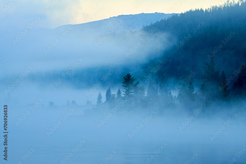 Fototapeta premium View over forest with morning fog. Dawn over the foggy lake Yazevoe. Beautiful dreamy view. Lake Yazevoe is located at an altitude of 1685 meters above sea level. Eastern Kazakhstan. Blur effect.