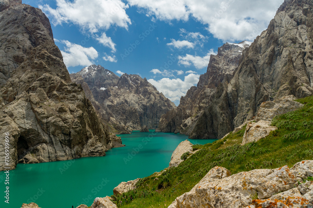 High-altitude Kel-Su Lake, China border, turquoise waters, rocky mountains, green vegetation, cloudy sky, natural beauty