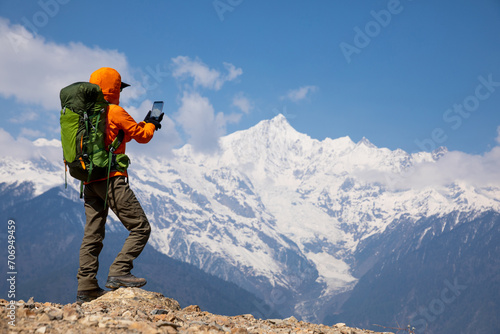 Woman backpacker taking photo of high altitude mountains with smart phone