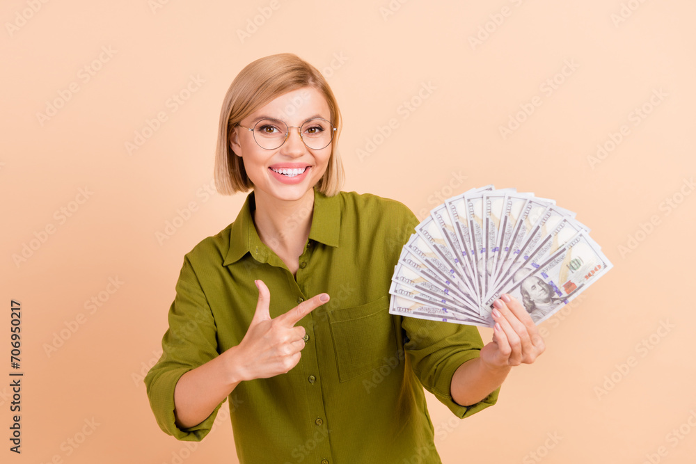 Portrait of positive gorgoeus clever girl wear khaki shirt in eyewear indicating at dollars in hand isolated on pastel color background Portrait of positive gorgoeus clever girl wear khaki shirt in eyewear indicating at dollars in hand isolated on pastel color background
