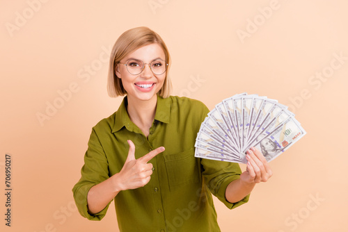 Portrait of positive gorgoeus clever girl wear khaki shirt in eyewear indicating at dollars in hand isolated on pastel color background photo