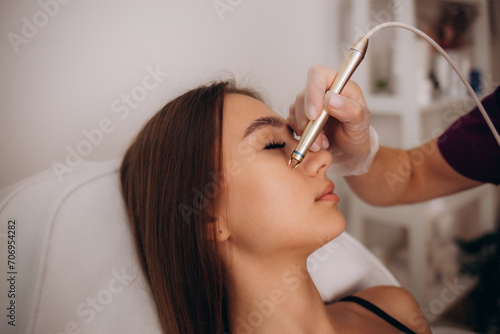 The cosmetologist makes the procedure treatment of Couperose of the facial skin of a beautiful, young woman in a beauty salon.Cosmetology and professional skin care. photo