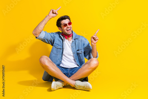 Full body photo of impressed man dressed denim shirt shorts sit directing look at sale empty space isolated on yellow color background