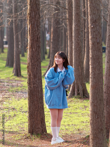 Foto Beautiful young Chinese woman posing in sunny summer forest, wearing blue loose oversized top and miniskirt with small shoulder bag