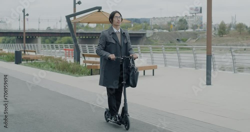 Slow motion of young Asian businessman riding electric scooter in city center. Modern urban transport and active lifestyle concept.