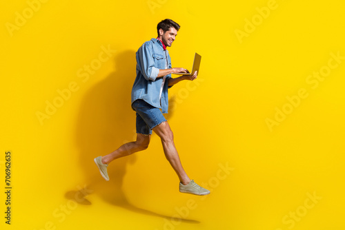 Full size photo of smart guy wear jeans jacket red scarf run empty space typing email on laptop isolated on yellow color background