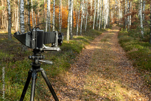 Large format view camera on a tripod standing on a forest road with filter holder attached to the lens. Analog photography hobby. photo