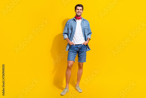 Full size photo of confident positive guy wear jeans jacket shorts standing arms in pockets isolated on bright yellow color background
