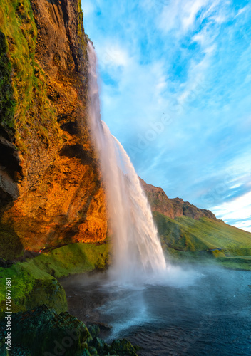 Seljalandsfoss is an impressive cascade on the south coast of Iceland. Majestic waterfall in warm evening sun in midsummer. Colorful scenery and major tourist attraction in wild volcanic nature.