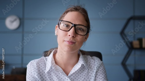 young brunette woman in white shirt and with earphones and eyeglasses on online conference call, consultation or webinar. smiles, listens and nods. Webcam view photo